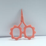 Sunflower-shaped embroidery scissors in peach powder coating, 2.5'' forged stainless steel, ideal for precision thread cutting and embroidery work.